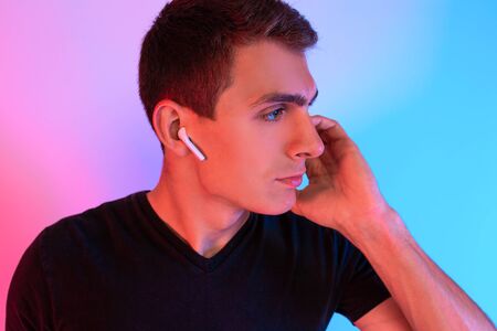 Portrait of an attractive young man, wearing wireless headphones, posing standing against a...