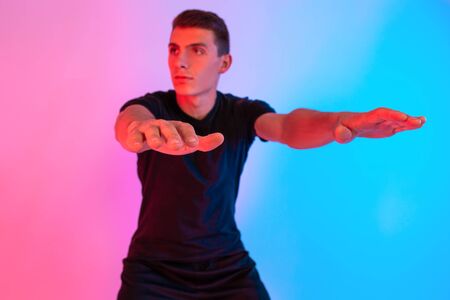 Young fitness man with headphones doing stretching exercises on background with red and blue neon...