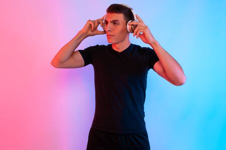 Attractive sporty man posing standing in the background with red and blue neon light listening to...