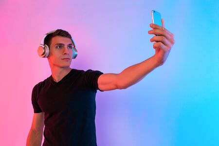 Sporty man with headphones taking selfie on your smartphone standing on background with red and blue neon light. The concept of sportの写真素材