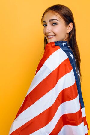 American dream. Young beautiful girl in a white t-shirt with the American flag, on a yellow background.の写真素材