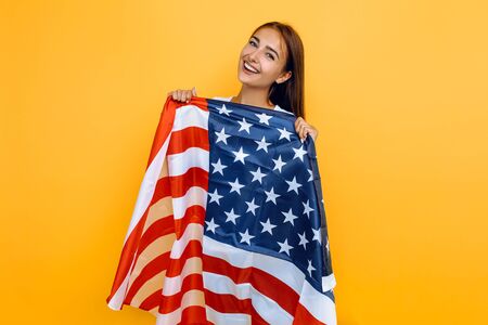 American dream. Young beautiful girl in a white t-shirt with the American flag, on a yellow background.の写真素材