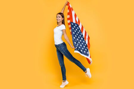 American dream. Young beautiful girl in a white t-shirt with the American flag, on a yellow background.の写真素材