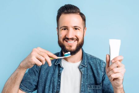 Happy young man with bristles, holding a brush and a tube of toothpaste, brushing his teeth immediately after waking up. Hygiene, morning routine and the concept of teeth whiteningの写真素材
