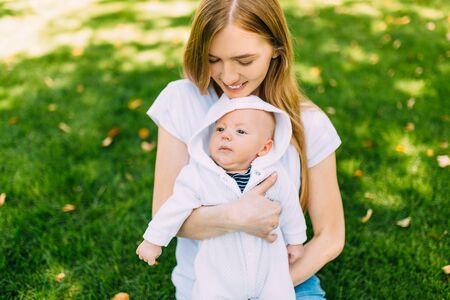Young beautiful woman mom holding a newborn baby in her arms, outdoors in summer
