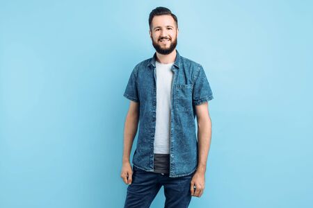 Happy fashionable handsome man with a beard posing standing on an isolated blue background