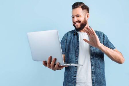 A happy smiling man holds a laptop and gives a thumbs up, approving gesture while standing on an...
