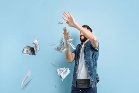 Portrait of a happy young bearded man throwing out banknotes isolated on a blue backgroundの写真素材