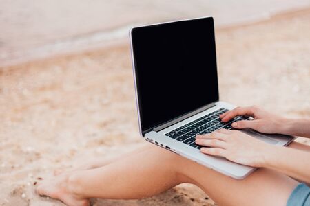 The girl is working working on a laptop sitting on the sand on the beachの写真素材