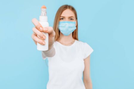 A young girl in a protective medical mask on her face, holding a disinfectant, hand antiseptic, on...