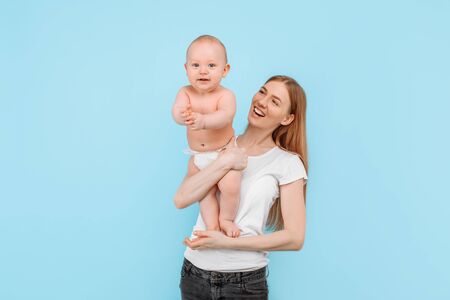 Happy family. a laughing mother gently lifts her adorable newborn son into the air, against an isolated blue backgroundの写真素材