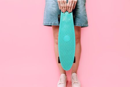 Close- up of a girl holding a skateboard on an isolated pink backgroundの写真素材