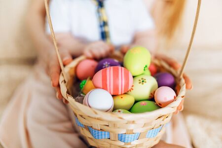 Happy Easter. Close-up of a happy mother and small children's hands holding colored eggs in a basket at homeの写真素材