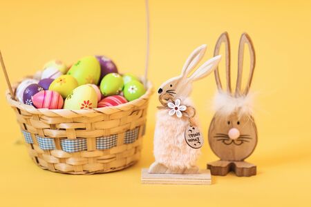 Wooden Easter Bunny with Easter eggs, on an isolated yellow background. Concept of Easter...