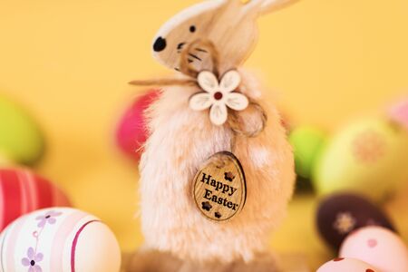 Wooden Easter Bunny with Easter eggs, on an isolated yellow background. Concept of Easter...