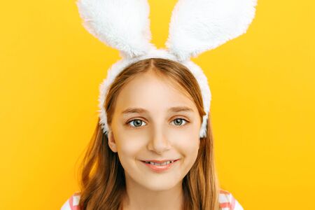 Happy little beautiful girl on her head with rabbit ears, posing on a yellow background. Symbol of...