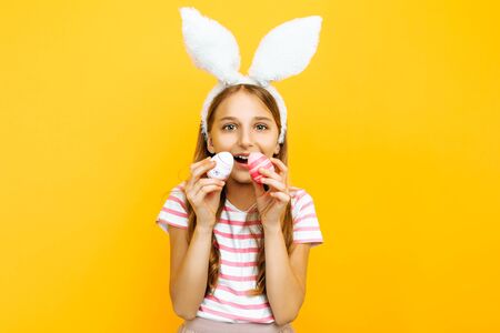 Beautiful happy girl on her head with rabbit ears and colorful Easter eggs in her hands, on a yellow background. Symbol of Easter and springの写真素材