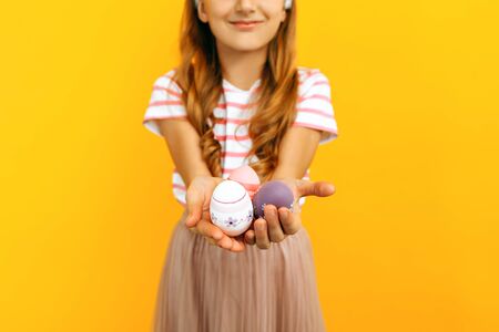 Beautiful happy girl on her head with rabbit ears and colorful Easter eggs in her hands, on a yellow...