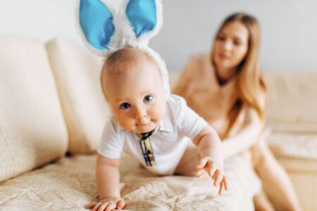 Happy Easter. A mother and a small baby, with rabbit ears on Easter day, have fun, play and cuddle while sitting on the sofa. Family celebrates Easterの写真素材