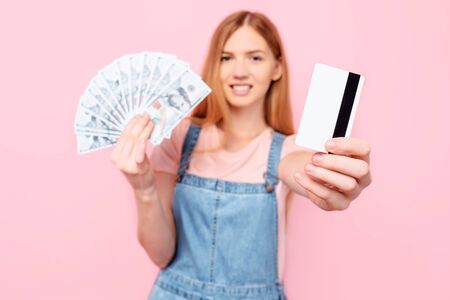 Portrait of a smiling successful young girl showing a lot of money in banknotes and holding a credit...