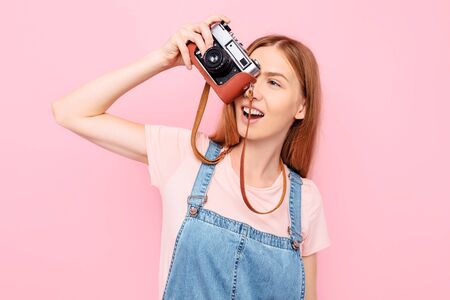 Attractive stylish young girl takes photos with a retro camera isolated on a pink background