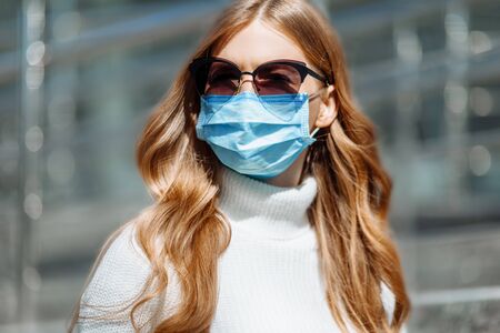 Beautiful young girl in a mask from coronovirus, student on the background of educational envy, women returning from work, remote work, in sun protective glasses, covid-19, with a laptop in her handsの写真素材