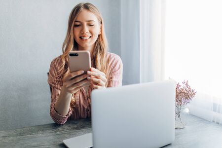 A young businesswoman works at home, sitting at a table with a mobile phoneの写真素材