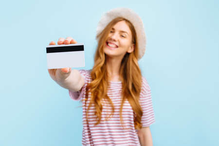 Portrait of a lovely young woman in summer hat showing a credit card and looking into copy space...