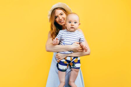 Happy family vacation in summer. Young happy mother holds a small child in her arms, on a yellow...