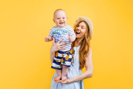 Happy family vacation in summer. Young happy mother holds a small child in her arms, on a yellow background. Family holidays, summer, travelの写真素材