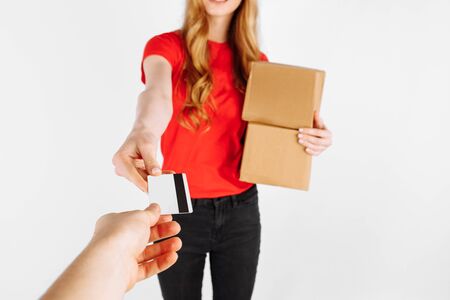 Courier girl in uniform holding cardboard boxes and a credit card on a white background. Delivery, payment by Bank transferの写真素材