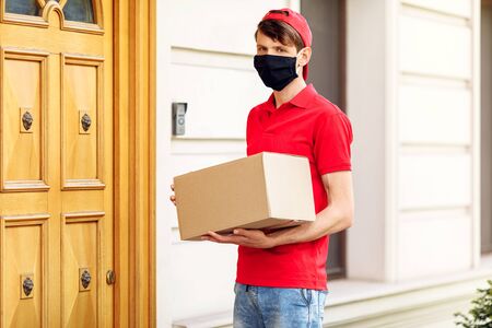 A courier in a protective medical mask with boxes in his hands delivers parcels. Service delivery in terms of quarantine, pandemic coronavirusの写真素材