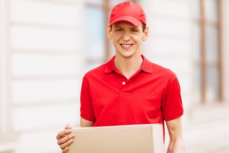 A happy uniformed Courier holds an empty cardboard box in the open air. Delivery serviceの写真素材