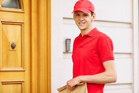 A courier in a red uniform holds a paper bag with food, the Concept of providing services