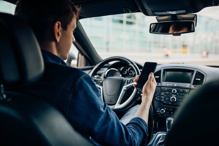 The man sitting behind the wheel of a car, using a mobile phone while driving a carの写真素材