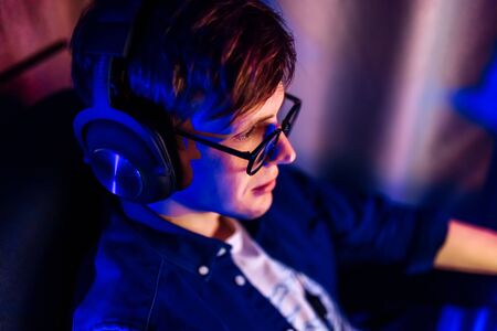 A happy young gamer with glasses and a headset plays computer games at home. Technology, games, entertainmentの写真素材
