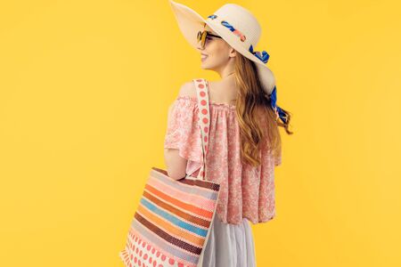 Stylish summer young woman in a summer hat, standing with her back to the camera on a yellow backgroundの写真素材