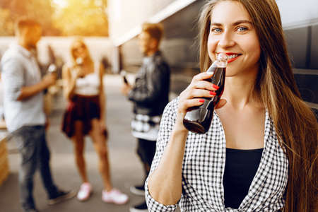 Closeup of a beautiful brunette girl with a drink, in the background a group of friends having funの写真素材