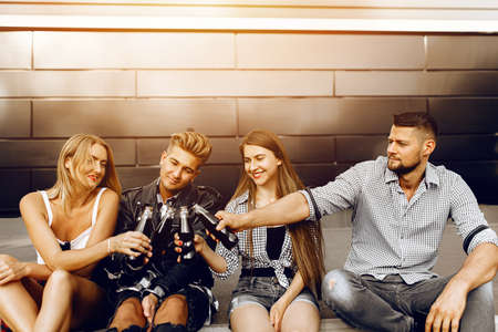 A group of stylish happy friends, girls and guys walk together around the city sitting on the...