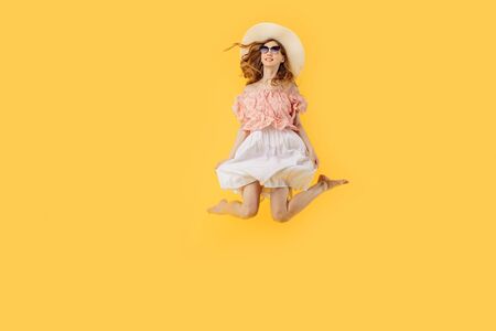 Full-length photo of a happy girl in a summer hat and sunglasses in summer, jumping high on an...