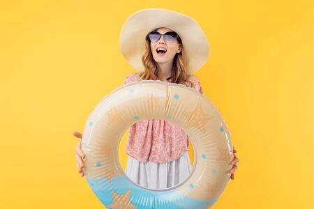 A shocked beautiful young woman in a straw hat standing in a floating inflatable ring and smiling...