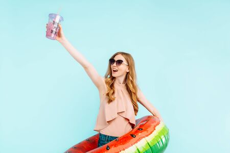 happy beautiful girl dressed in a swimsuit and sunglasses holds an inflatable swimming circle and a...