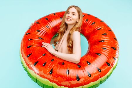 Happy beautiful girl dressed in a swimsuit and a summer cap, holding an inflatable swimming ring, on...