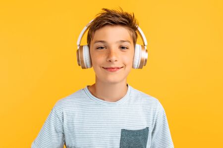 Smiling teenager listening to music on headphones, standing on an isolated yellow background