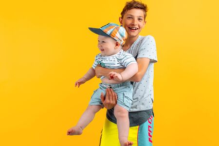 happy family, a teenage boy in summer clothes holding his younger brother in his arms, on an isolated yellow backgroundの写真素材