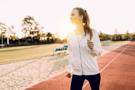 Athletic young woman in sportswear running around the stadium at dawnの写真素材