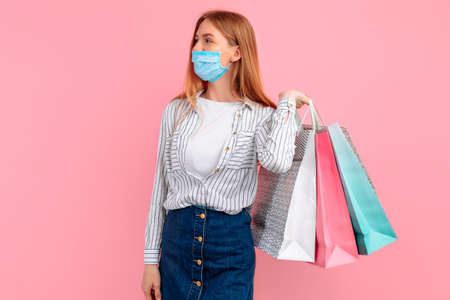 Happy young woman in a medical mask on her face, gives a thumbs up and smiles cheerfully, I like it, on a pink backgroundの写真素材