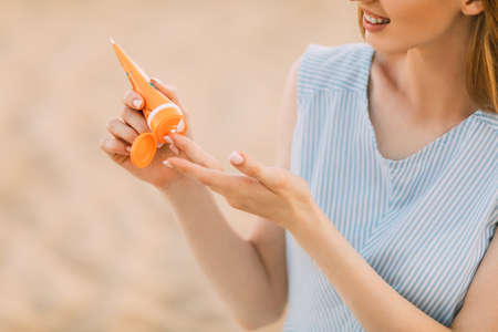 Woman's hands with sunscreen lotion, against the background of the sea. Summer vacation