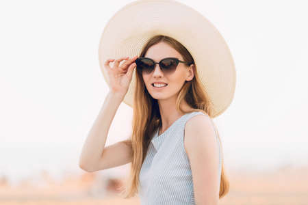 Portrait of a beautiful summer girl in sunglasses and a summer hat, relaxing and posing on the...