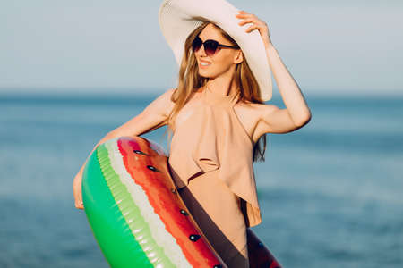beautiful girl in a summer cap and swimsuit is smiling happily, relaxing on the beach and posing with an inflatable swimming circle in the form of a watermelon. Summer holidayの写真素材